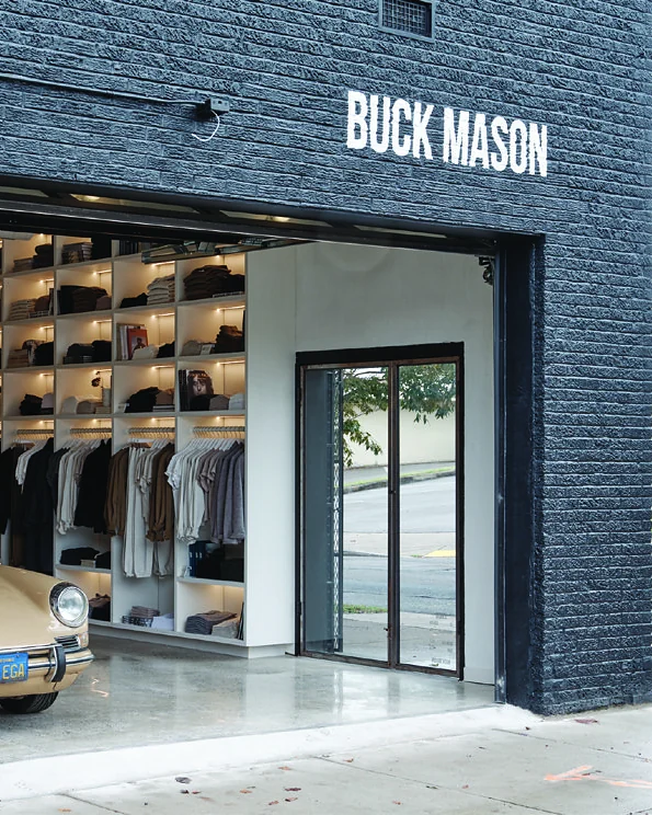 Buck Mason storefront — brick pier, full signage and an open shopfront onto the sidewalk