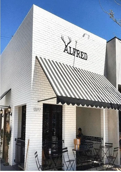 White brick corner cafe with a striped awning and sidewalk seating